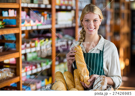 Smiling female staff holding loaf of bread at bread counter Smiling female staff holding loaf of bread at bread counter 27426985