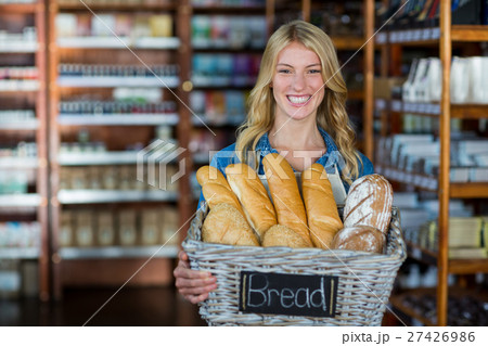 Smiling female staff holding a basket of breads Smiling female staff holding a basket of breads 27426986