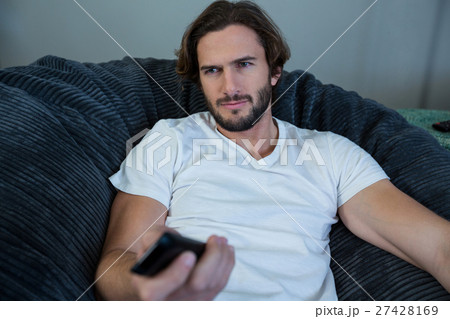 Man changing a channel while watching tv in living room 27428169
