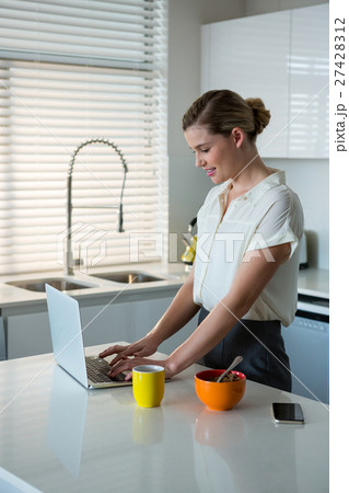 Woman using laptop in kitchen Woman using laptop in kitchen 27428312