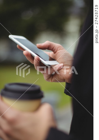 Mid section of businesswoman using mobile phone while holding disposable coffee cup Mid section of businesswoman using mobile phone while holding disposable coffee cup 27428719
