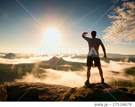 Sportsman shadowing eyes from bright sun, summit 27516678