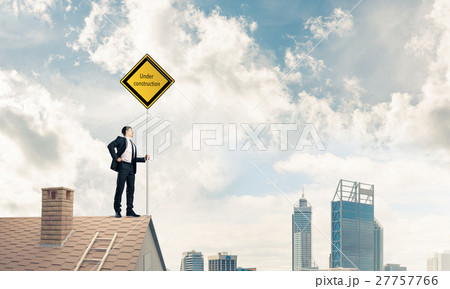 Young businessman on house brick roof holding yellow signboard a 27757766