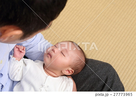 寝ている赤ちゃんと抱っこして覗き込む父親の写真素材