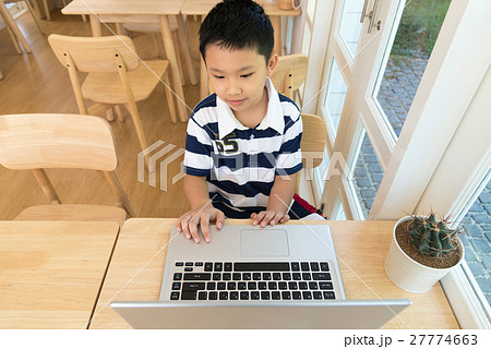 Asian boy sitting at his desk with laptop computer Asian boy sitting at his desk with laptop computer 27774663