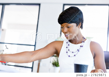 Young woman sitting at a desk in an office and working on blueprint 27829871