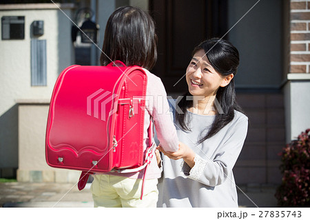 お見送りをする母親と赤いランドセルを背負った小学生の女の子の写真素材
