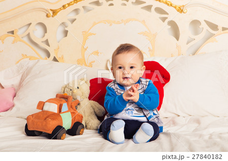Cute toddler boy sitting on the bed and playing Cute toddler boy sitting on the bed and playing 27840182