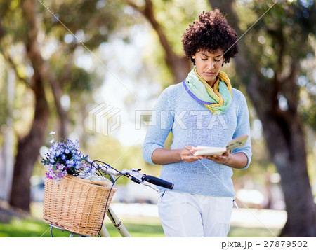 Happy young woman with bicycle reading book Happy young woman with bicycle reading book 27879502