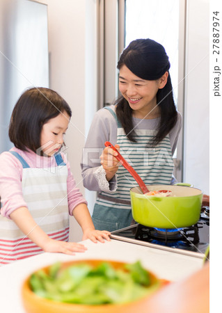 キッチンで料理をする母親とお手伝いをする女の子の写真素材