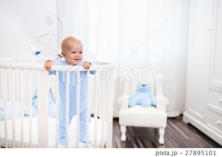 Baby boy standing in bed in white nursery Baby boy standing in bed in white nursery 27895101