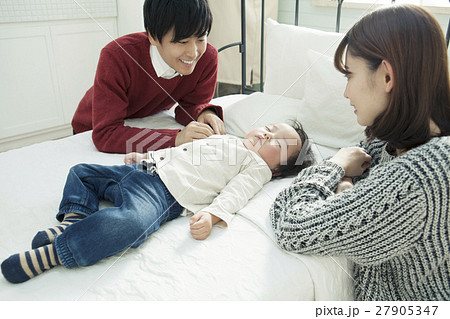 子供の寝顔を見る夫婦の写真素材