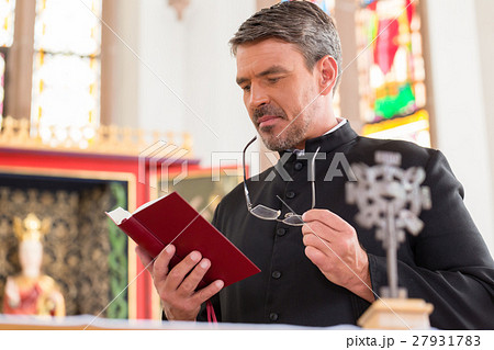 Priest reading bible in church standing at altar Priest reading bible in church standing at altar 27931783