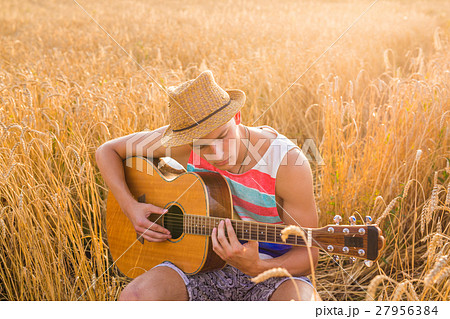 Happy handsome man is playing guitar in the field 27956384