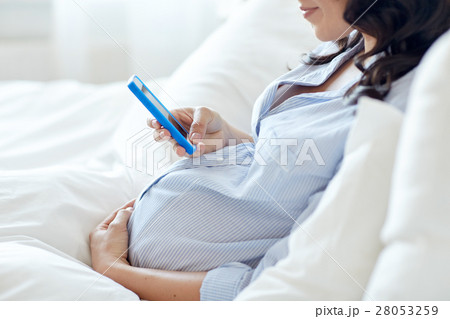 close up of pregnant woman with smartphone in bed 28053259