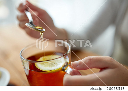 close up of woman adding honey to tea with lemon 28053513
