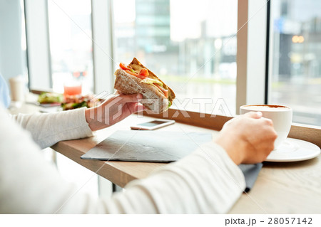 woman eating sandwich and drinking coffee at cafe 28057142