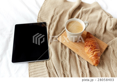 tablet pc, coffee and croissant on bed at home 28058403