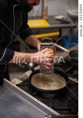 Cropped shot of male chef grating cheese on pan 28156844
