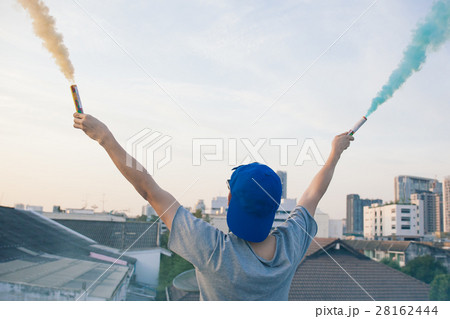 Male teenager holding colorful smoke sticks in air 28162444