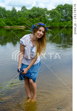 Woman on river bank squeezes wet hem of skirt 28178576
