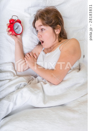 Young woman is waking up and looking at clock. 28183831