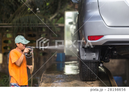 Man spraying pressure washer for car wash in car care shop. Focus on backside of car 28198656