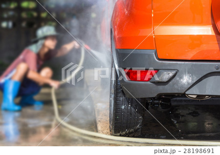 Man spraying pressure washer for car wash in car care shop. Focus on car 28198691