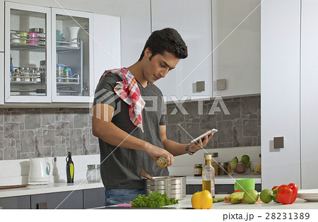 Young man cooking in kitchen using digital tablet 28231389