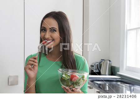 Close-up of a smiling woman eating vegetable salad Close-up of a smiling woman eating vegetable salad 28231406