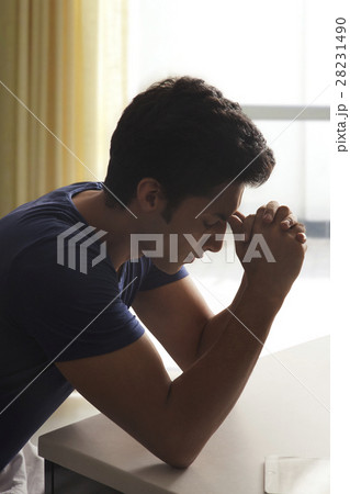 Young man sitting at kitchen table with hands on face 28231490