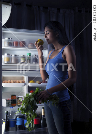 Young woman taking fruits and leafy vegetables from fridge  28231835