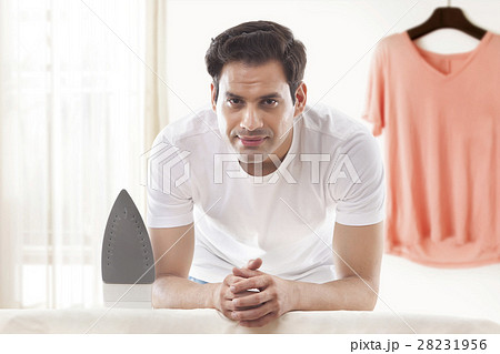 Portrait young man with ironing board and top hanging on wall at home Portrait young man with ironing board and top hanging on wall at home 28231956