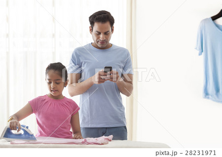 Daughter ironing clothes and father using mobile phone 28231971