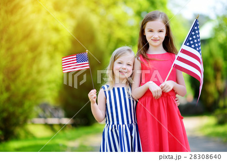 Two adorable little sisters holding american flags outdoors on beautiful summer day Two adorable little sisters holding american flags outdoors on beautiful summer day 28308640
