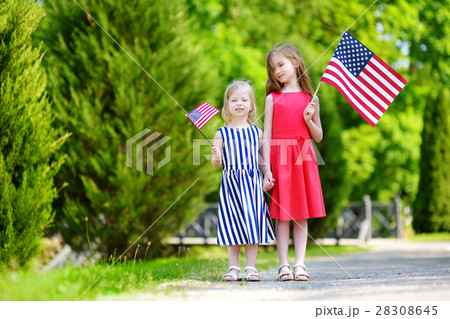 Two adorable little sisters holding american flags outdoors on beautiful summer day Two adorable little sisters holding american flags outdoors on beautiful summer day 28308645