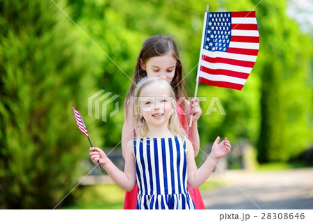 Two adorable little sisters holding american flags outdoors on beautiful summer day Two adorable little sisters holding american flags outdoors on beautiful summer day 28308646