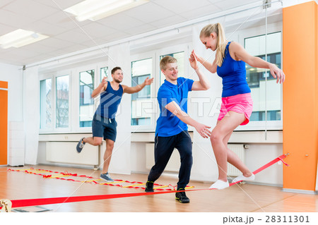 Physio practicing slacklining with athletes in gym 28311301