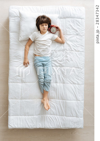 Relaxed boy lying in the bed with an alarm 28347342