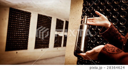 A women holds a bottle of wine in an aging cellar. 28364624