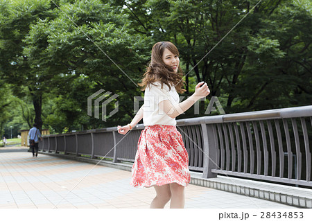 若い女性 振り返る 笑顔 揺れる髪 屋外 緑の写真素材