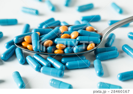 Blue capsules and orange pills in a spoon. 28460167