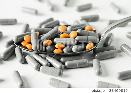 White capsules and orange pills in a spoon. White capsules and orange pills in a spoon. 28460816