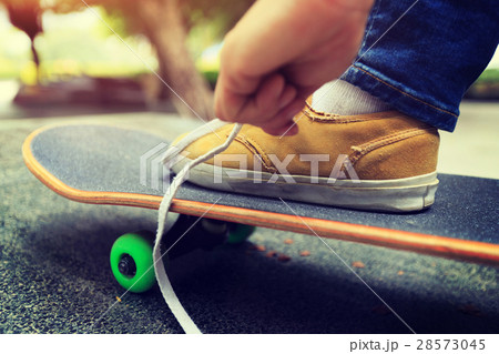 young skateboarder tying shoelace at skatepark 28573045