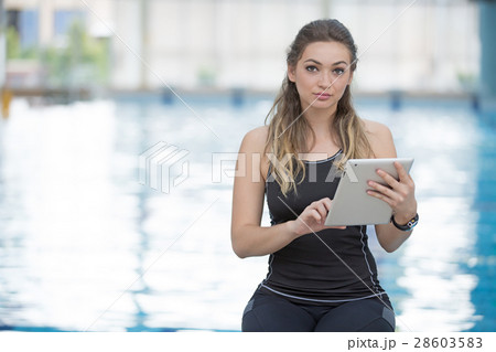 Fit female swimming trainer with tablet at the 28603583