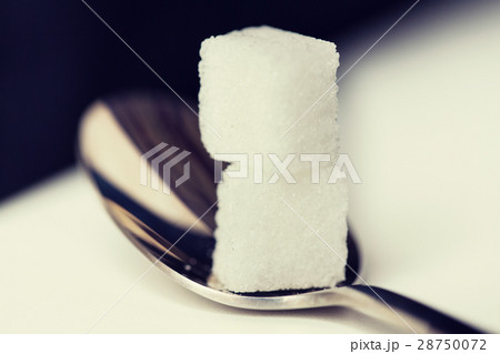 close up of white sugar cubes on teaspoon 28750072