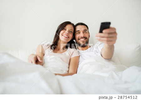 happy couple lying in bed at home and watching tv 28754512