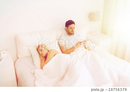 man texting message while woman is sleeping in bed man texting message while woman is sleeping in bed 28756379