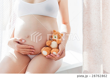 Pregnant woman with knitted toy teddy bear. 28762862