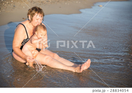 Naked baby on aged woman hands at beach Naked baby on aged woman hands at beach 28834054